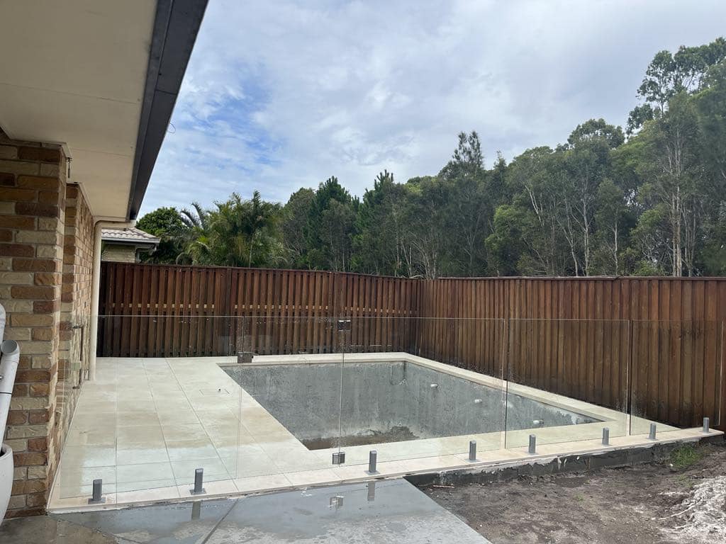 Frameless glass with silver spigots around a newly rendered plunge pool